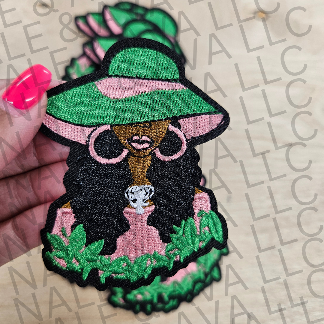 Embroidered patch of a dog wearing sunglasses and a hat held by a hand on a branded surface.