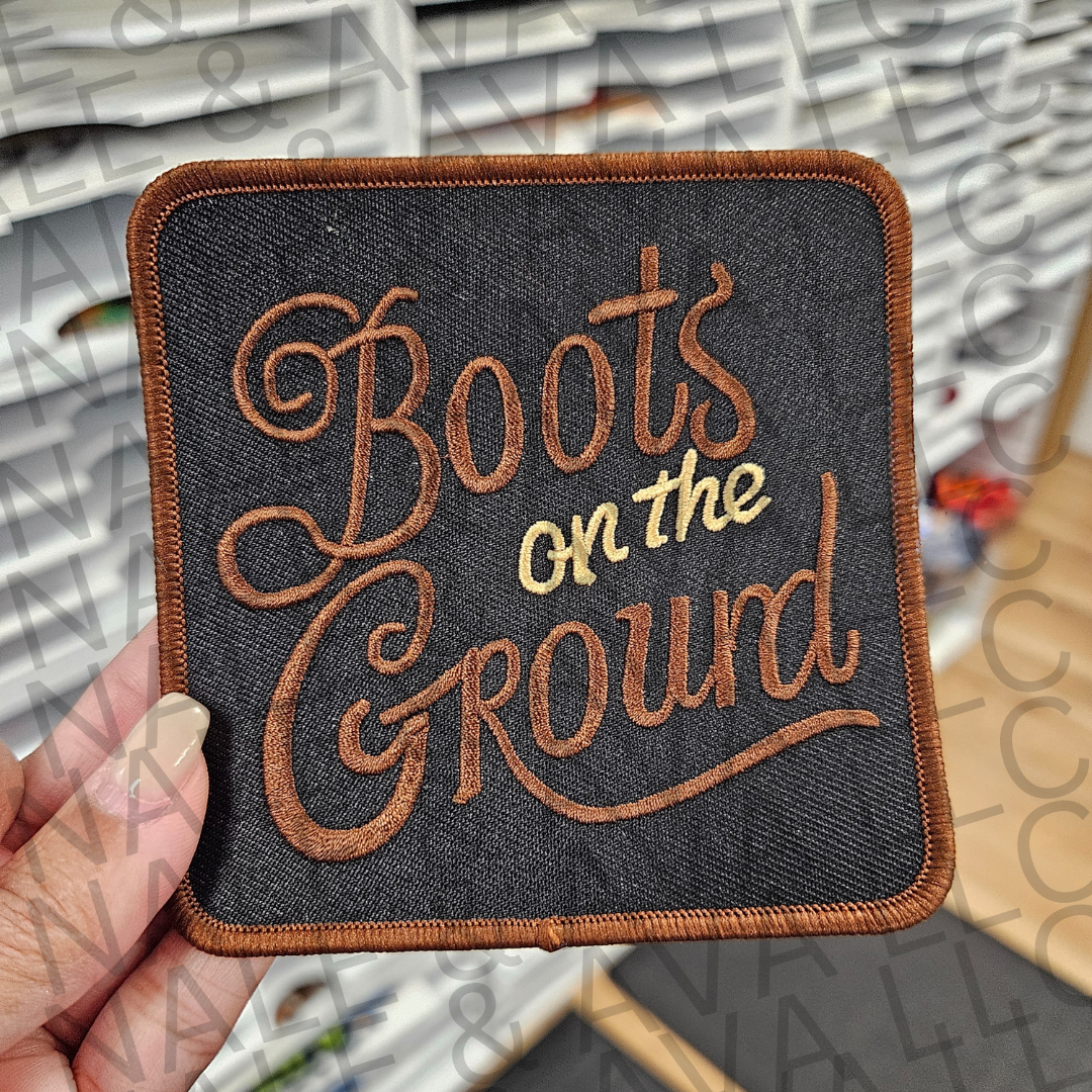 Patch with 'Boots on the Ground' text held by a hand against a blurred background