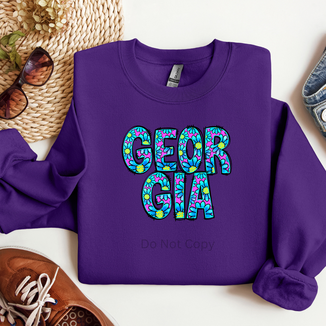 A purple crewneck sweatshirt with the word 'GEORGIA' printed in a stylized font consisting of blue and green colors.