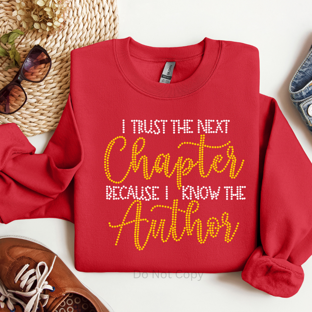 Red sweatshirt with text 'I Trust the Next Chapter Because I Know the Author' on a white background