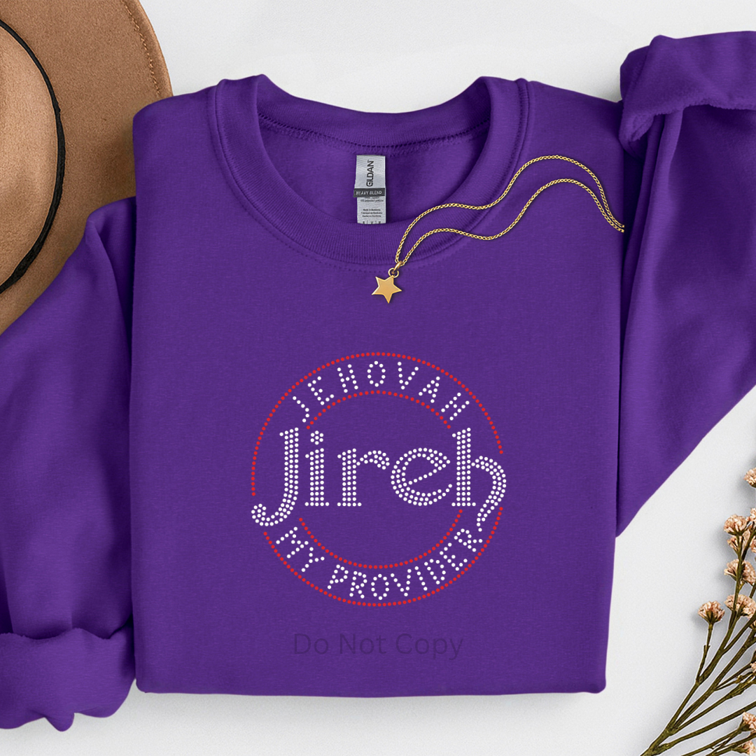 Purple sweatshirt with 'Jehovah Jireh My Provider' text, placed on a white surface with a hat and necklace.