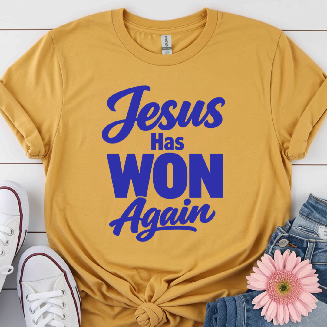 Yellow t-shirt with 'Jesus Has Won Again' text on a white wooden surface with shoes and a flower.