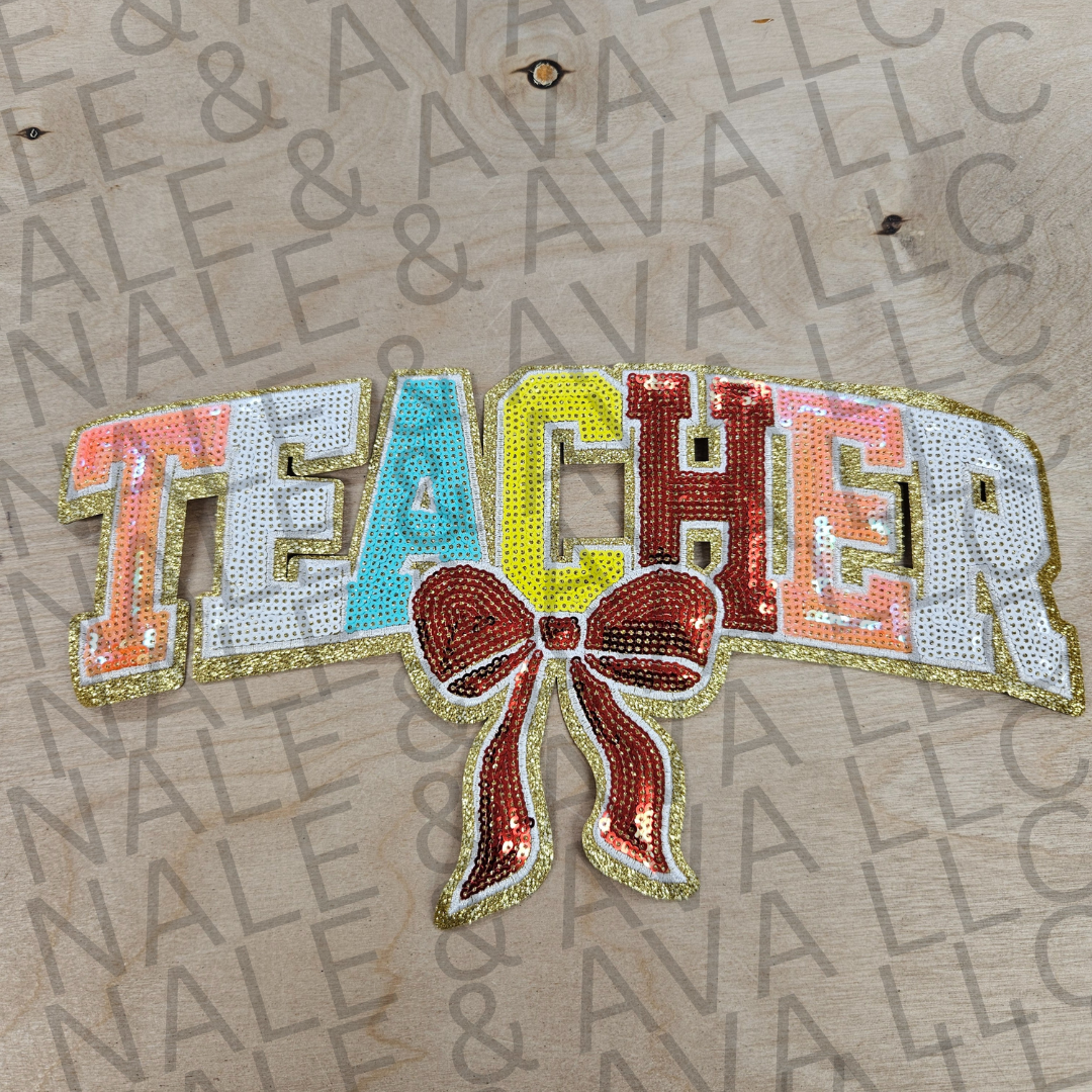 Decorative patch with 'TEACHER' text and a bow on a cardboard background