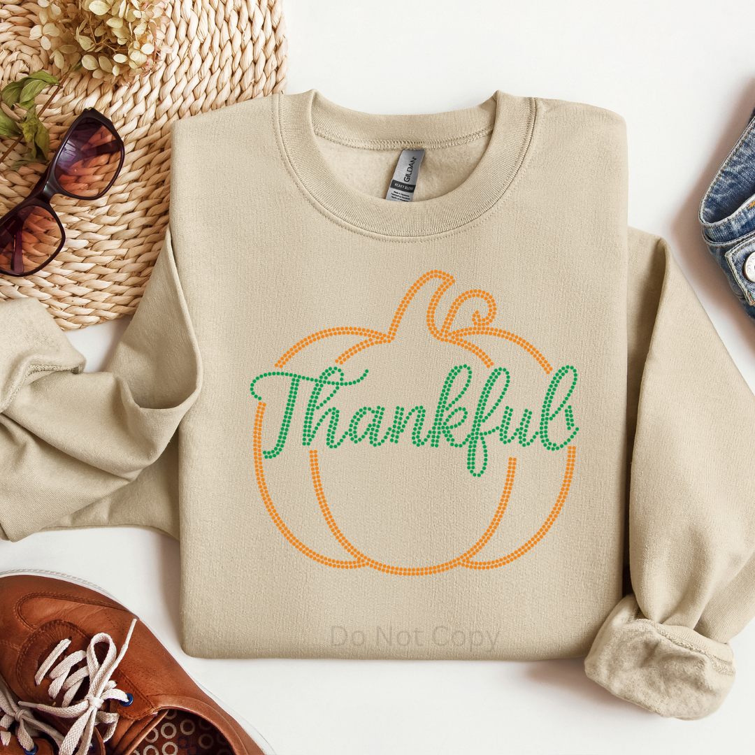Beige sweatshirt with 'Thankful' design on a white surface with accessories.