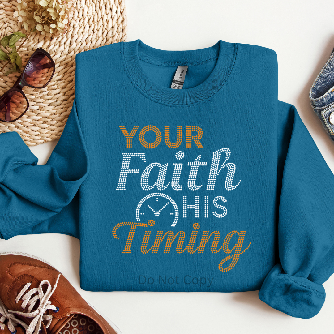 Blue sweatshirt with 'Your Faith, His Timing' text on a white surface with accessories.