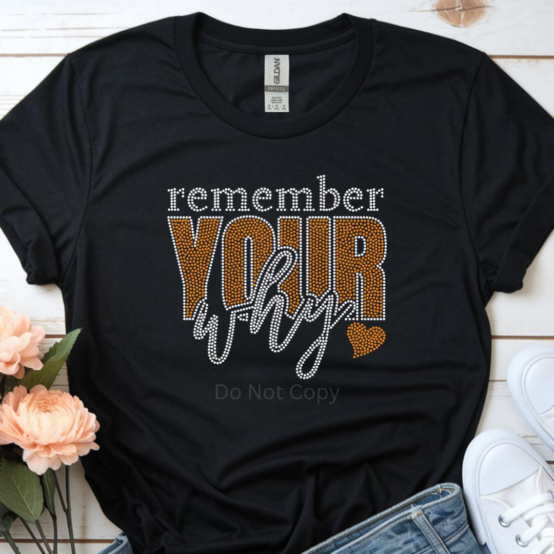 Black t-shirt with 'remember your why' text on a wooden surface with flowers and sneakers.