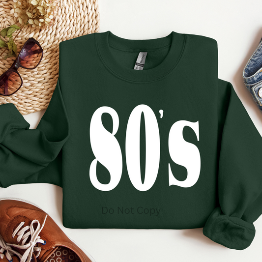Green sweatshirt with '80's Do Not Copy' text on a white surface with accessories.