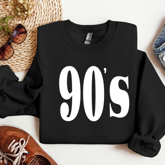 Black sweatshirt with '90s' text on a white surface with accessories around