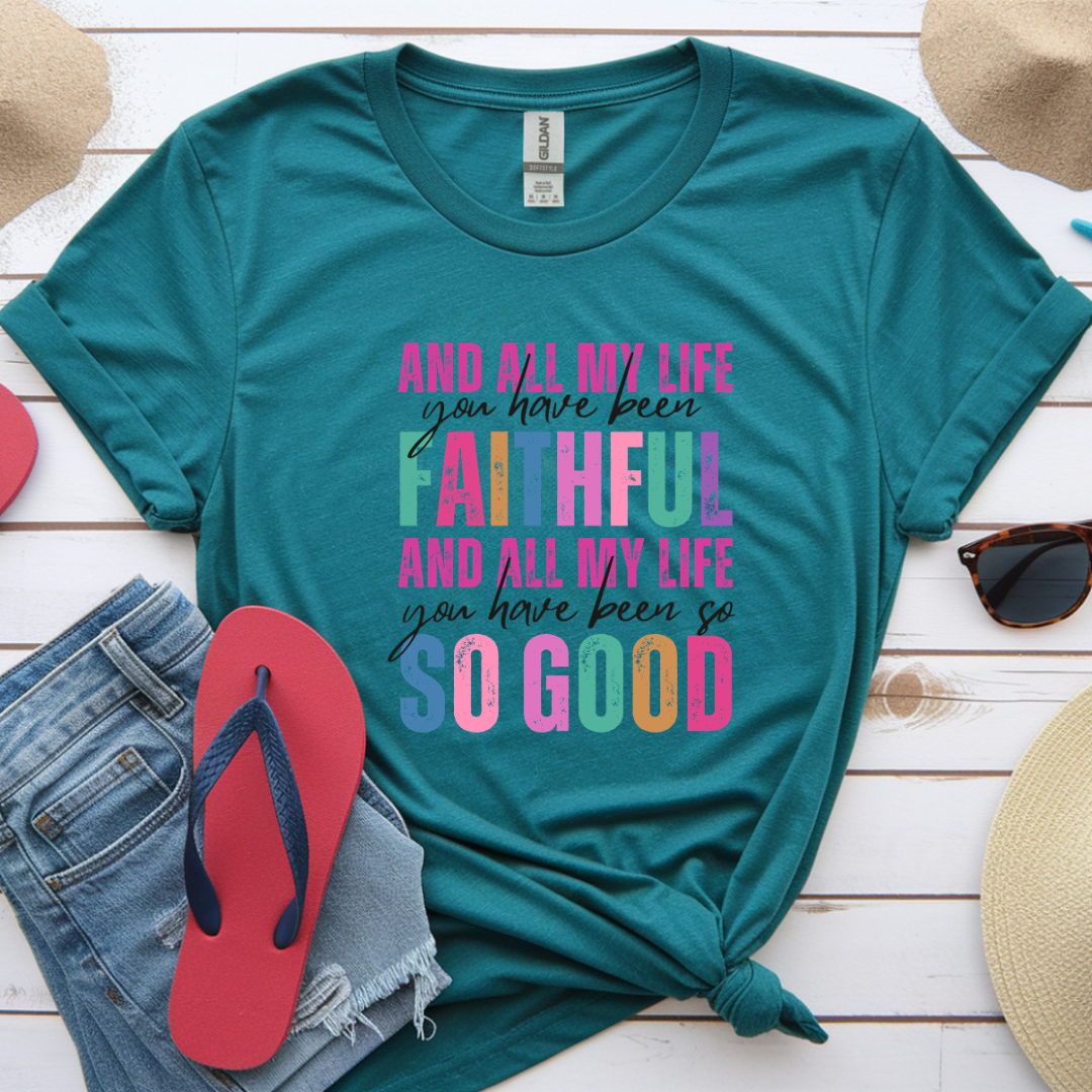 Teal t-shirt with colorful text on a wooden surface with accessories.
