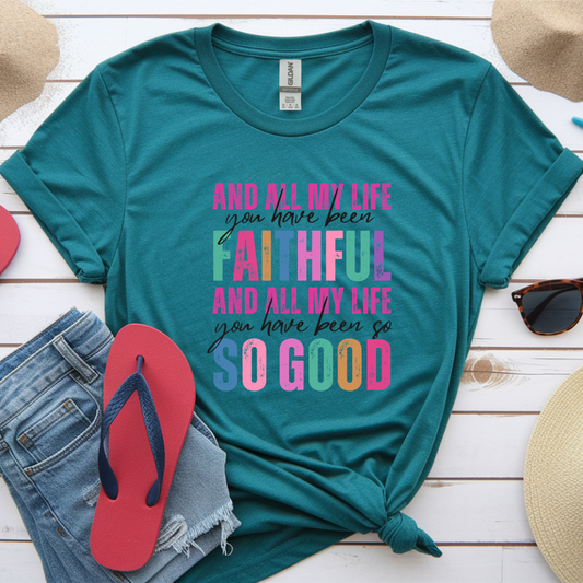 Teal t-shirt with colorful text on a wooden surface with accessories.