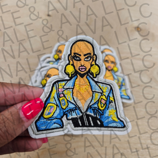 Patch of a stylized character with a blue jacket held by a hand against a branded background.