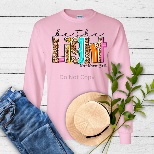A pink crewneck sweatshirt laid out flat with a graphic transfer design on it, alongside a fabric roller, leaves, and a straw hat.