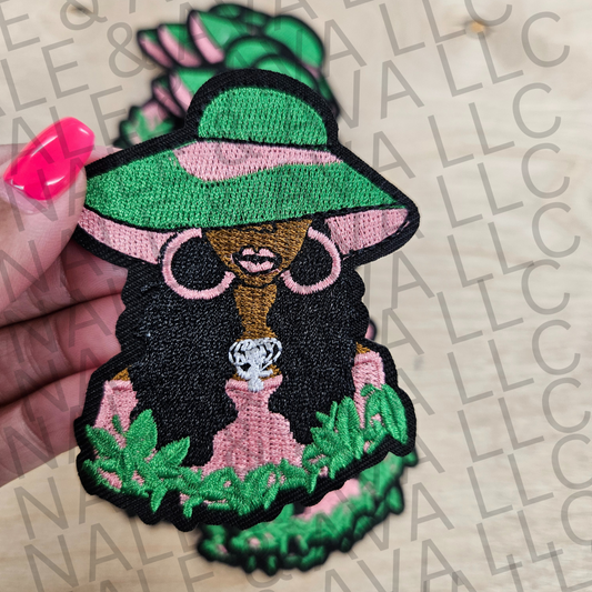 Embroidered patch of a dog wearing sunglasses and a hat held by a hand on a branded surface.