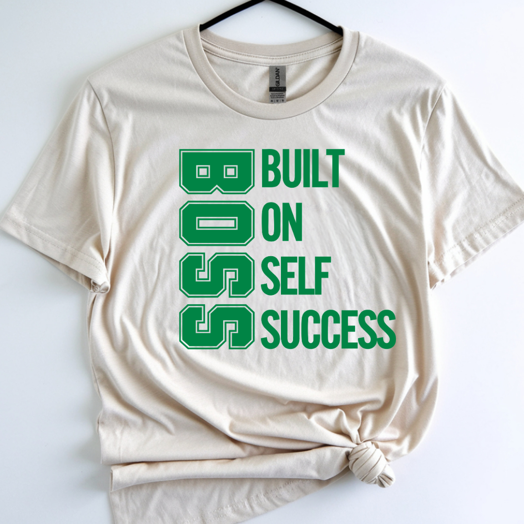 Beige t-shirt with green text 'BUILT ON SELF SUCCESS' on a white background