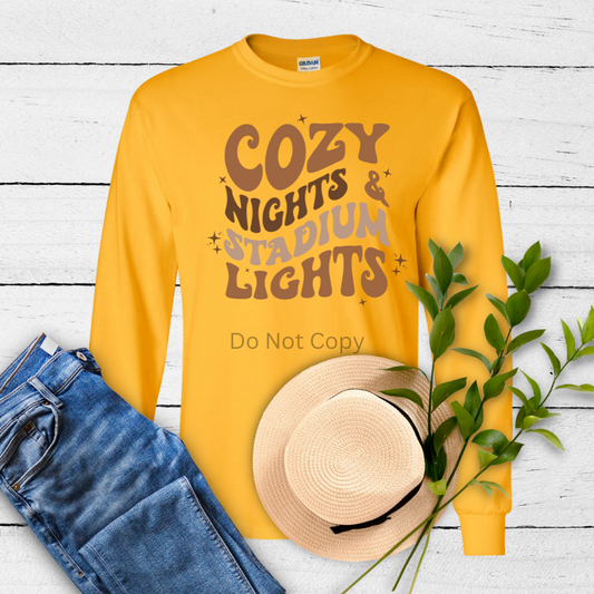 A yellow long-sleeved shirt with the text 'COZY NIGHTS & STADIUM LIGHTS' printed on the front.