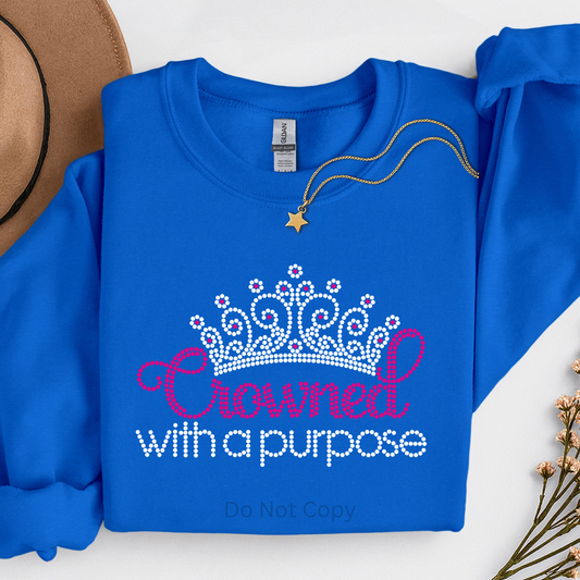 Blue sweatshirt with 'Crowned with a Purpose' text and tiara graphic, necklace on top, on a white background.
