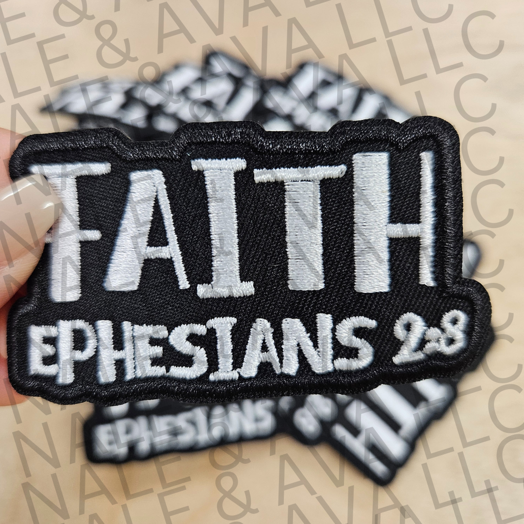 Black patch with 'FAITH Ephesians 2:8' text held by a hand on a patterned background