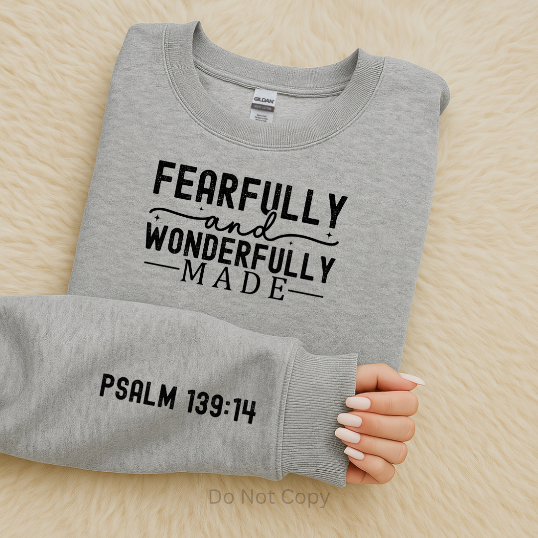 Gray sweatshirt with 'Fearfully and Wonderfully Made' text on a wooden surface