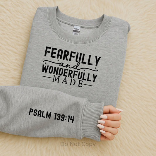 Gray sweatshirt with 'Fearfully and Wonderfully Made' text on a wooden surface