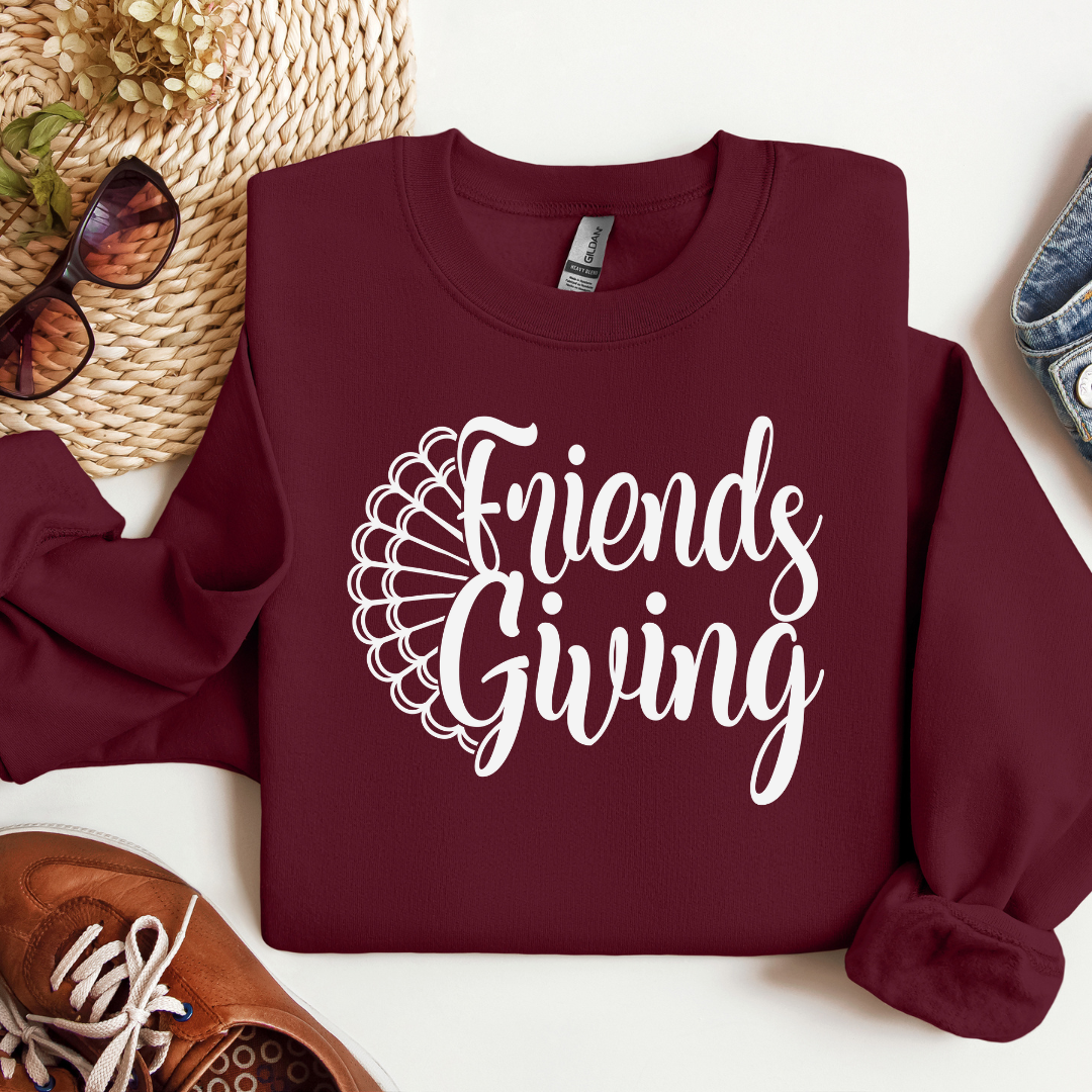 Maroon sweatshirt with 'Friends Giving' text on a white surface with accessories.