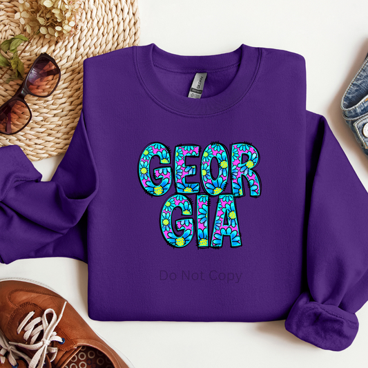 A purple crewneck sweatshirt with the word 'GEORGIA' printed in a stylized font consisting of blue and green colors.