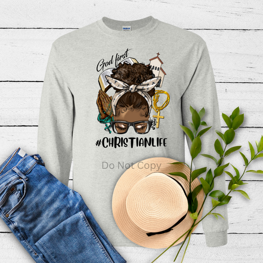 A gray sweatshirt with a graphic design that includes text and various symbols related to Christianity, accompanied by a hat, jeans, and decorative plants on a wooden background.