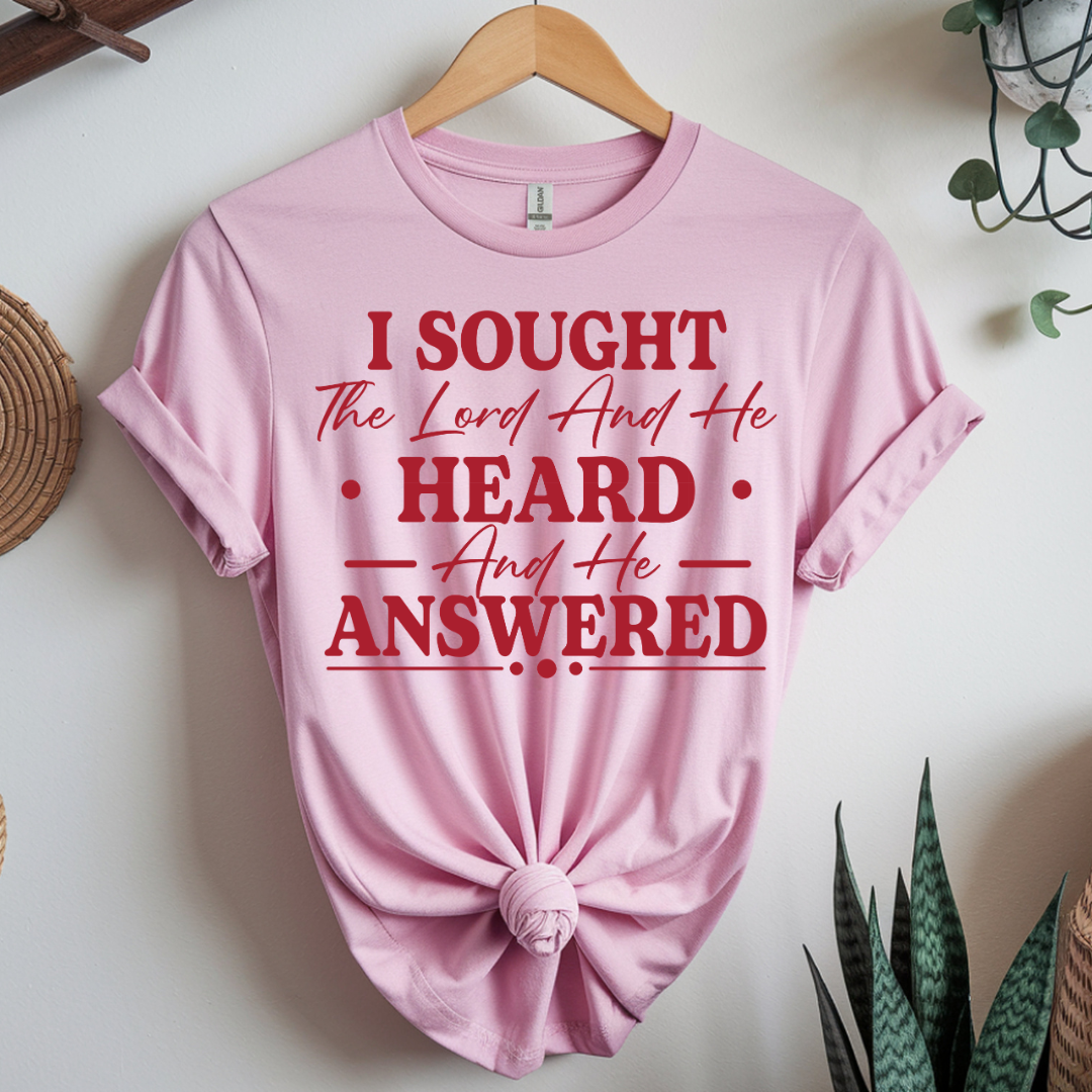 Pink t-shirt with red text on a hanger against a white wall.