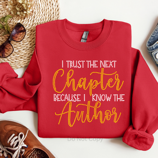 Red sweatshirt with text 'I Trust the Next Chapter Because I Know the Author' on a white background
