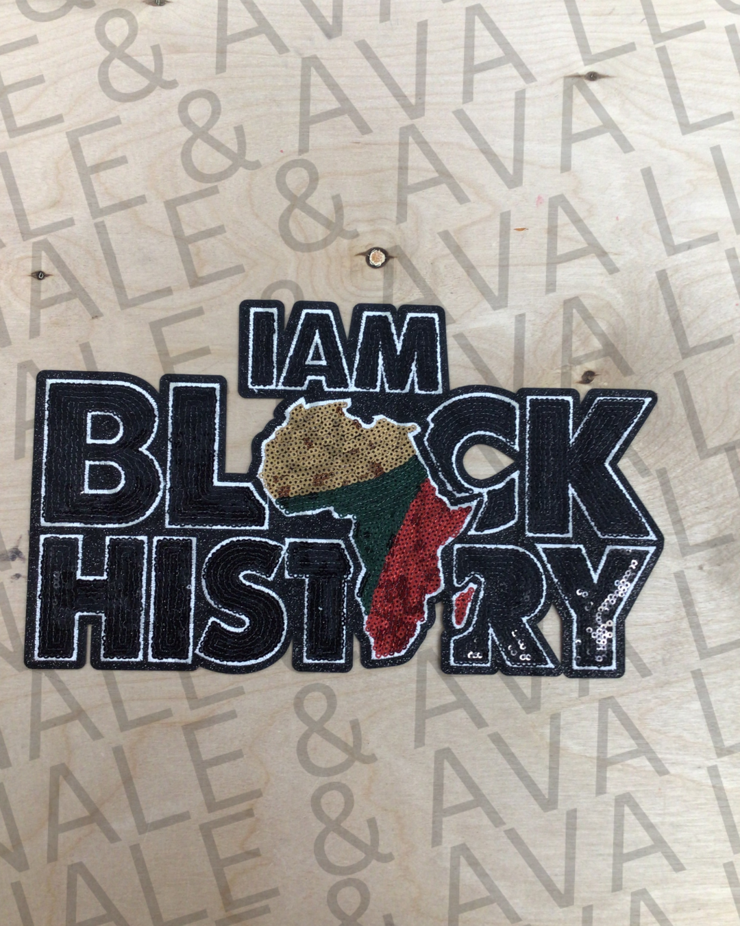 A sequin patch with the text 'I AM BLACK HISTORY' and an illustration of a stylized Africa map in the background, intended for application on a wooden surface.