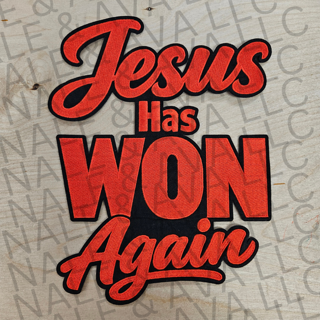 A decorative sign or sticker with the phrase 'Jesus Has WON Again' in red textured lettering with black outlines, displayed on a light wood background with a faint repeating watermark.