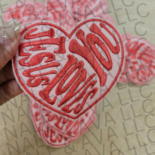 Heart-shaped patch with 'Jesus Loves You' text held over a blurred background