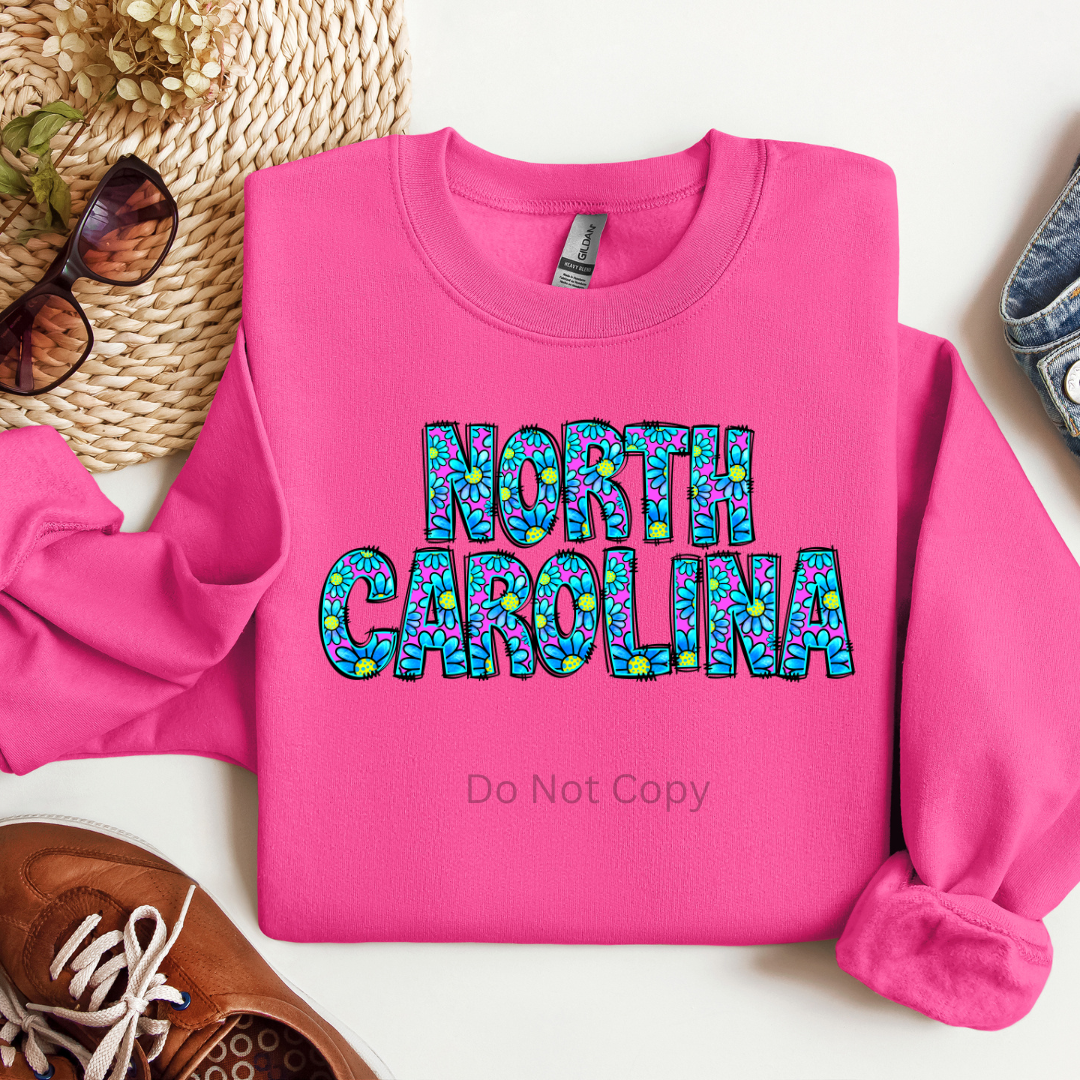 A pink sweatshirt with the text 'NORTH CAROLINA' in a decorative font, surrounded by a pattern.