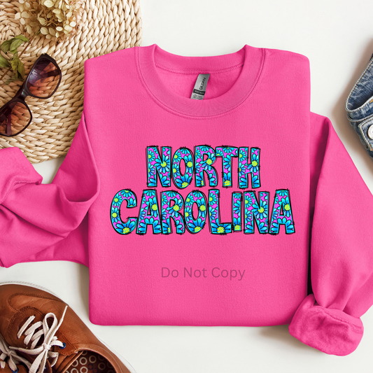 A pink sweatshirt with the text 'NORTH CAROLINA' in a decorative font, surrounded by a pattern.