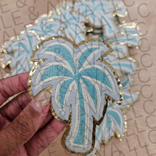 Embroidered palm tree patch held by a hand with a blurred background