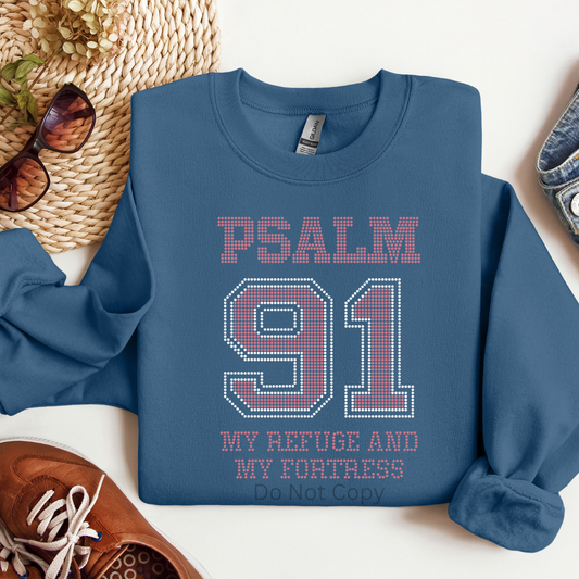 Blue sweatshirt with 'Psalm 91' text on a white surface with accessories around