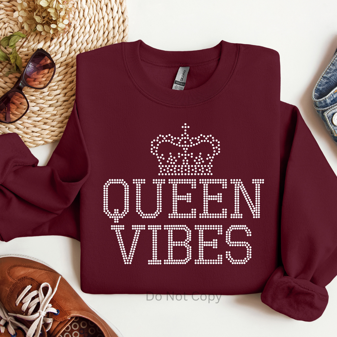 Maroon sweatshirt with 'QUEEN VIBES' text and crown design on a white surface with accessories.