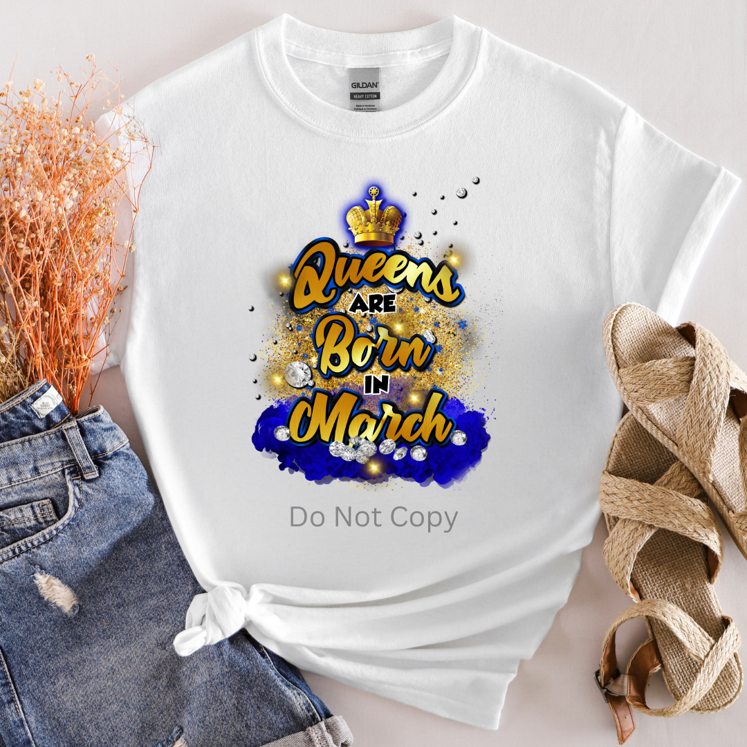 A white T-shirt with the text 'Queens are Born in March' in a decorative font, predominantly in gold with a blue background.