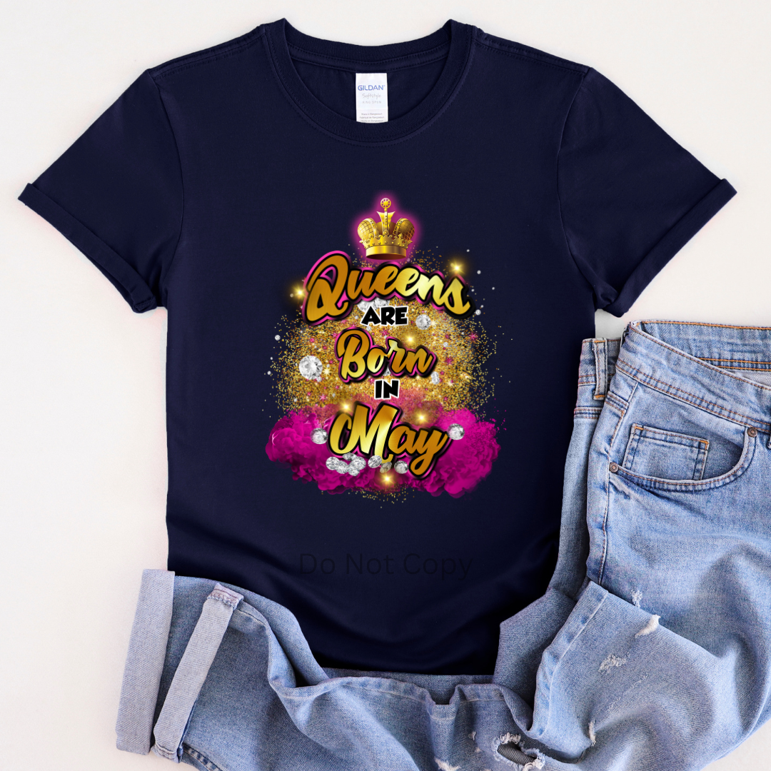 A navy blue T-shirt laid flat with a graphic transfer design that reads 'Queens are Born in May' accompanied by a crown and decorative elements.