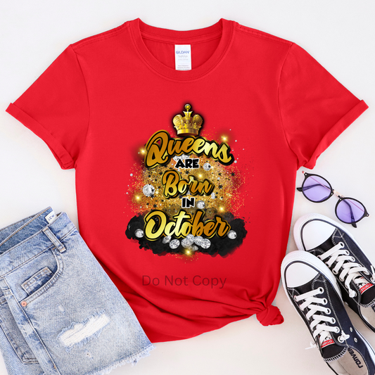 A red T-shirt with the text 'Queens are born in October' printed on it, accompanied by a crown illustration and decorative elements.