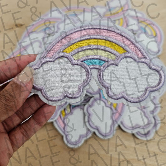 Hand holding a rainbow and cloud patch with 'Vale & Aveline' branding in the background.