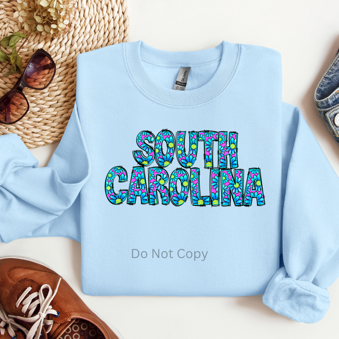 A light blue shirt with the text 'SOUTH CAROLINA' printed on it in a decorative font, surrounded by a pattern of what appears to be leaves or flowers in various colors.