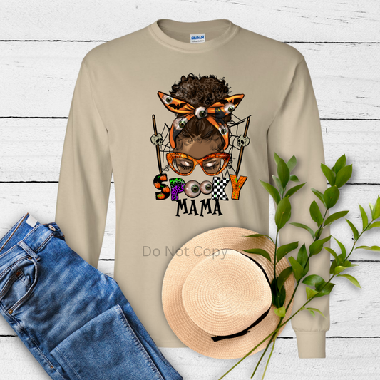 A beige long-sleeved shirt with the text 'Spooky Mama' and an image of a cartoonish character wearing glasses and a bow.