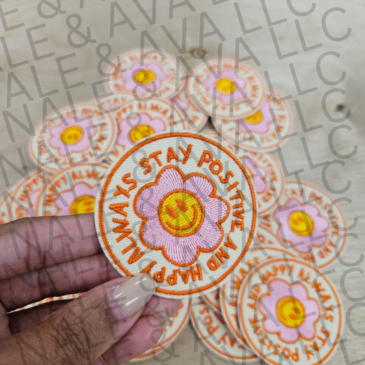 Circular patch with 'Always Stay Positive and Happy' text held by a hand, surrounded by similar patches on a patterned background.