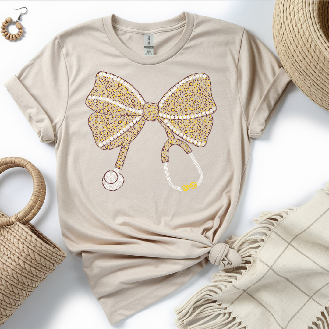 Beige t-shirt with a leopard print bow design on a white surface with accessories.
