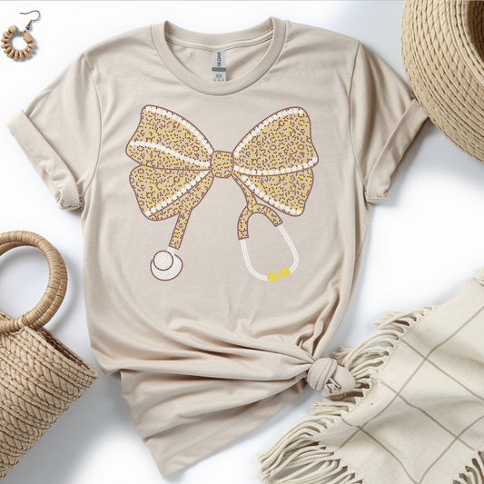 Beige t-shirt with a leopard print bow design on a white surface with accessories.