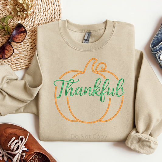 Beige sweatshirt with 'Thankful' design on a white surface with accessories.