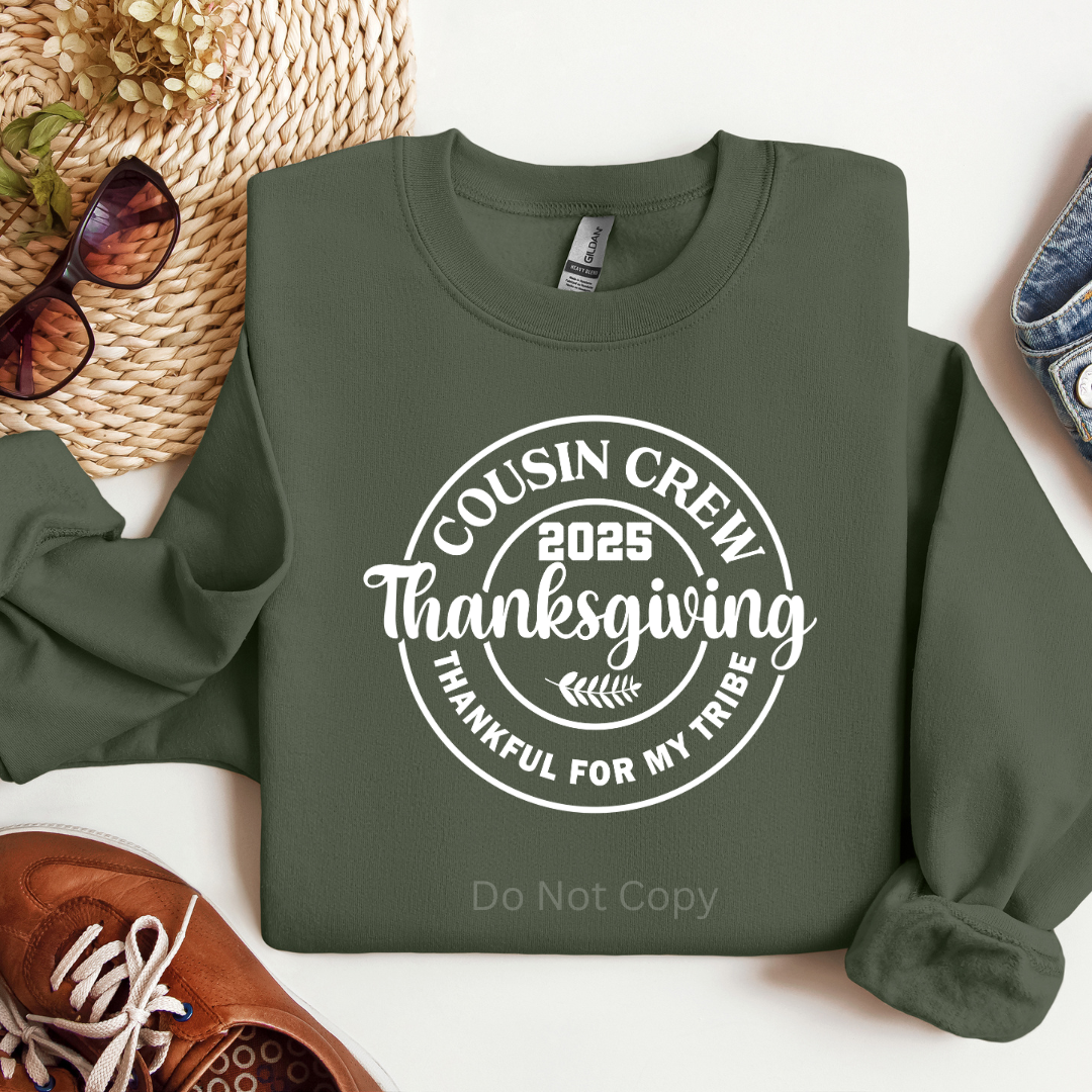 Green sweatshirt with 'Cousin Crew 2025 Thanksgiving' text on a white surface with accessories.