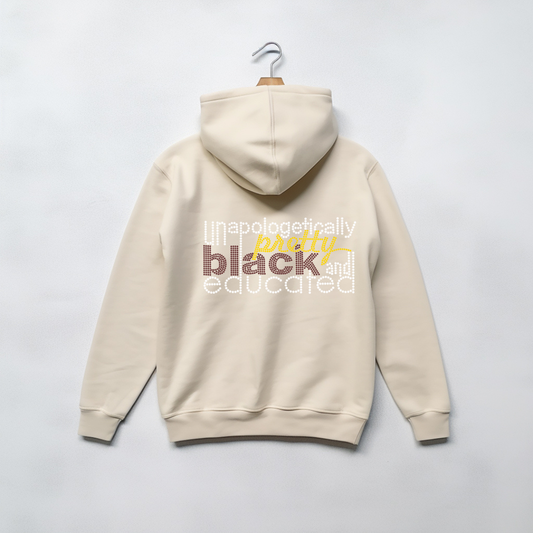 A cream-colored hoodie hanging on a wooden hanger against a light gray background, featuring a graphic text print on the back in white, yellow, and brown.