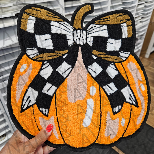 Decorative patch with a pumpkin and checkered bow design held by a hand.