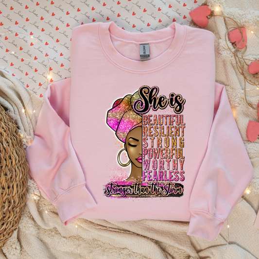 A pink sweatshirt with a graphic DTF transfer design showing a woman's silhouette and text attributes like beautiful, resilient, strong, powerful, worthy, and fearless.